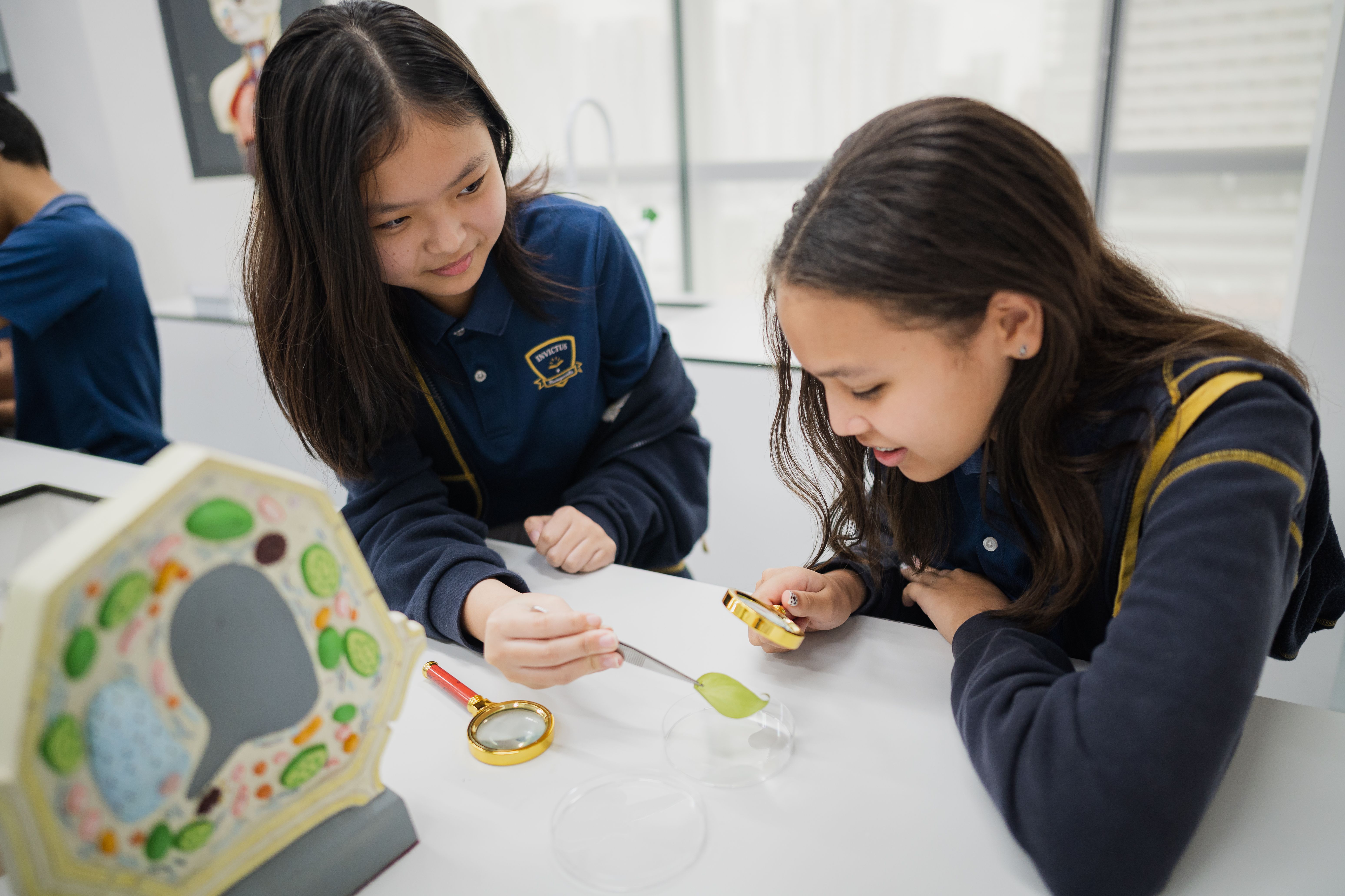 Secondary students at Invictus International School examining a leaf with magnifying glasses during a hands-on biology lesson as part of the Cambridge Lower Secondary science curriculum.