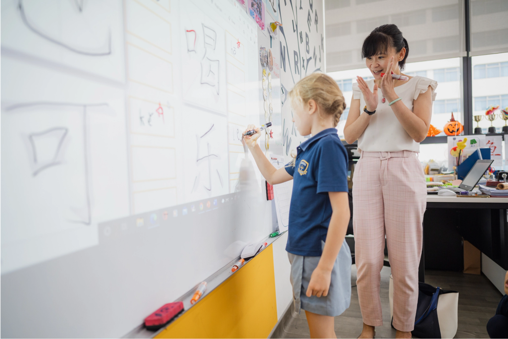 Teacher cheering as a student is writing Mandarin characters on a white board