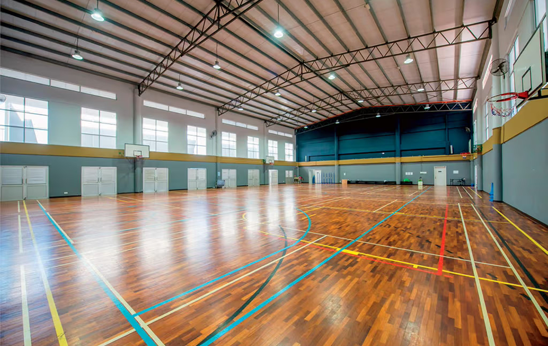 Spacious indoor sports hall at Spring Hills Campus with polished wooden flooring, marked courts, and basketball hoops, designed for multi-sport activities.