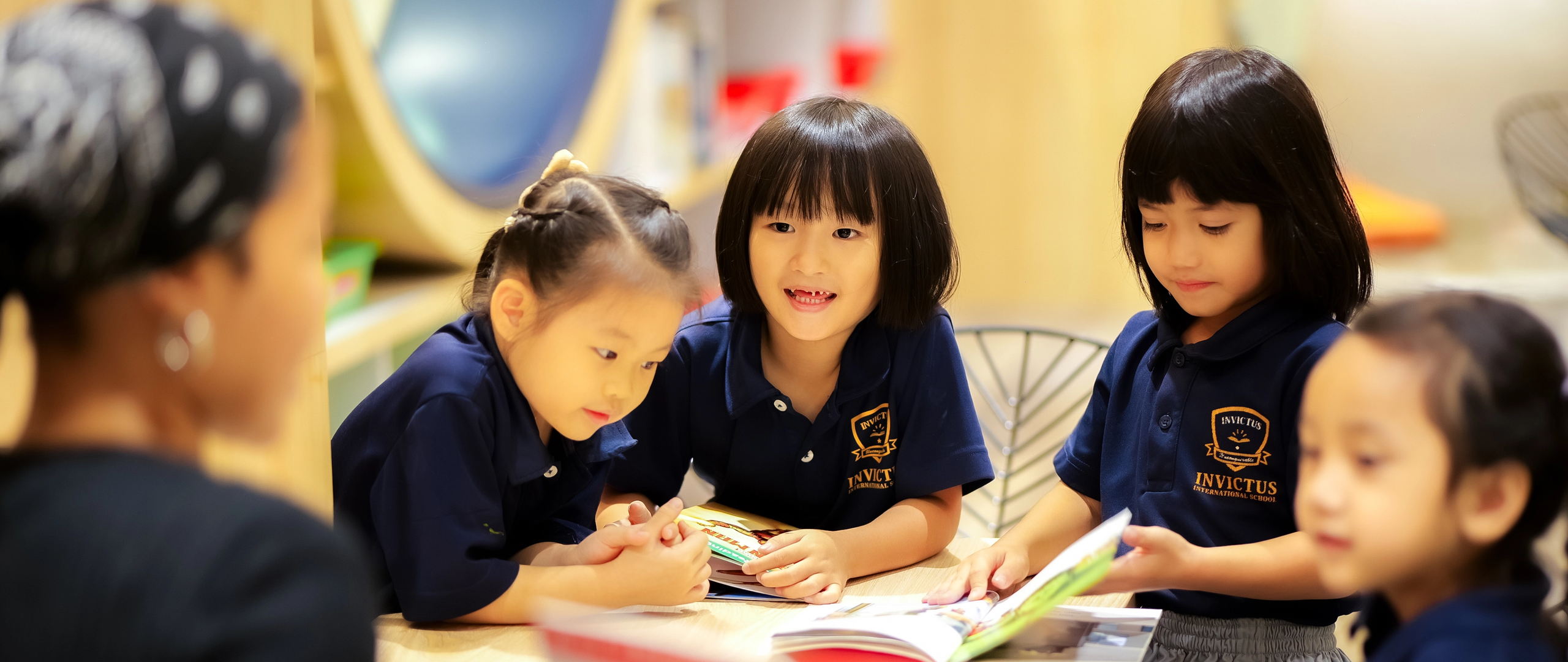 Invictus Early Years students listen to a story read by their teacher, engaging with books in a nurturing, language-rich classroom environment.