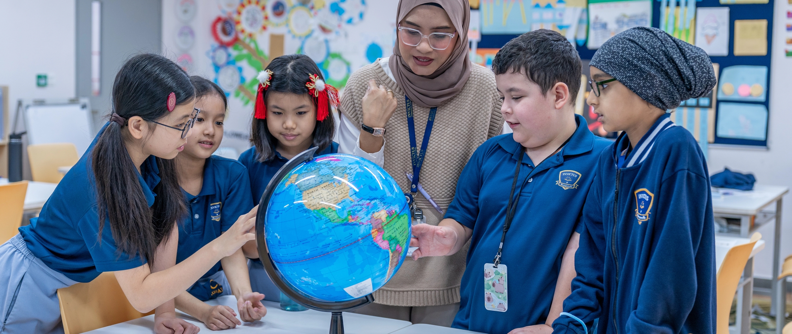 Multicultural cohort of Invictus students standing around a globe and having a discussion with teacher