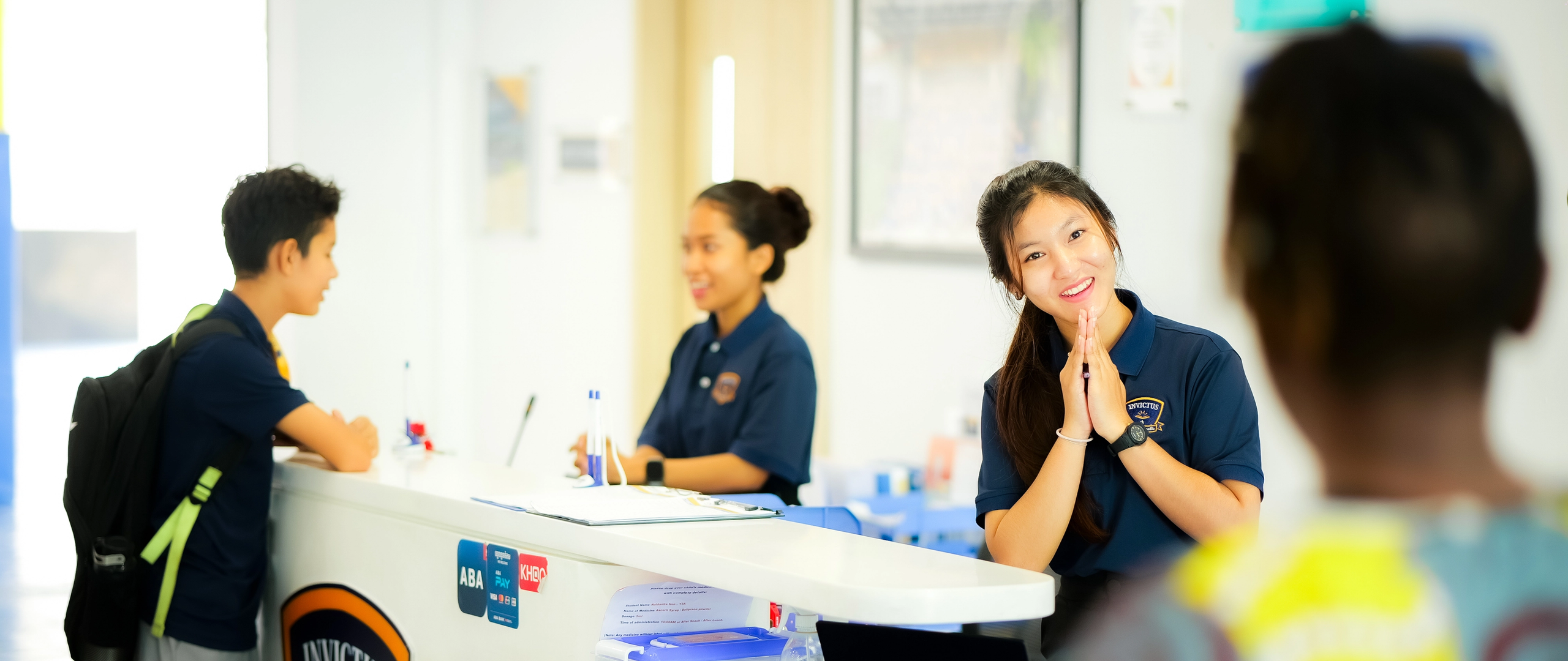 Invictus staff warmly greet a student and parent at the school reception counter, reflecting a welcoming and supportive admissions environment.Invictus staff warmly greet a student and parent at the school reception counter, reflecting a welcoming and supportive admissions environment.