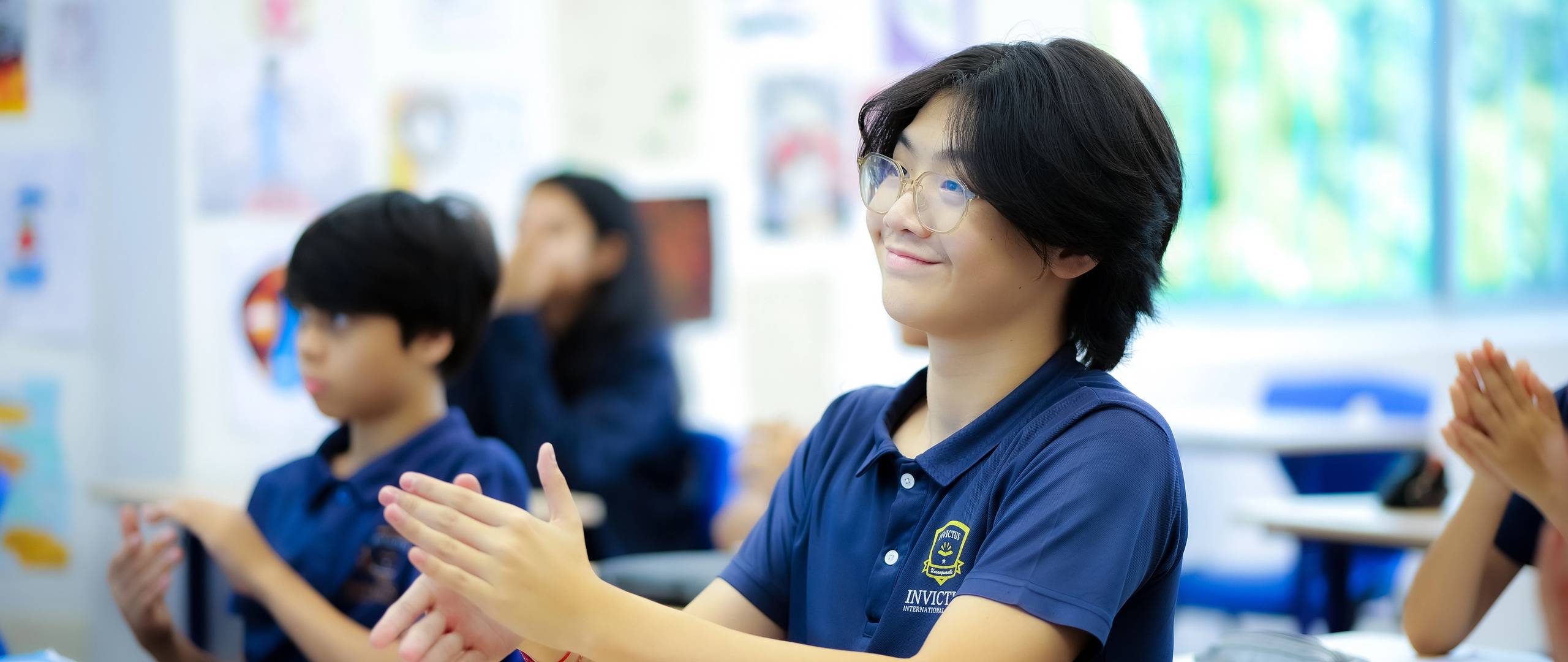 A smiling secondary student applauds in class at Invictus International School, showing appreciation and participation in a collaborative learning environment.
