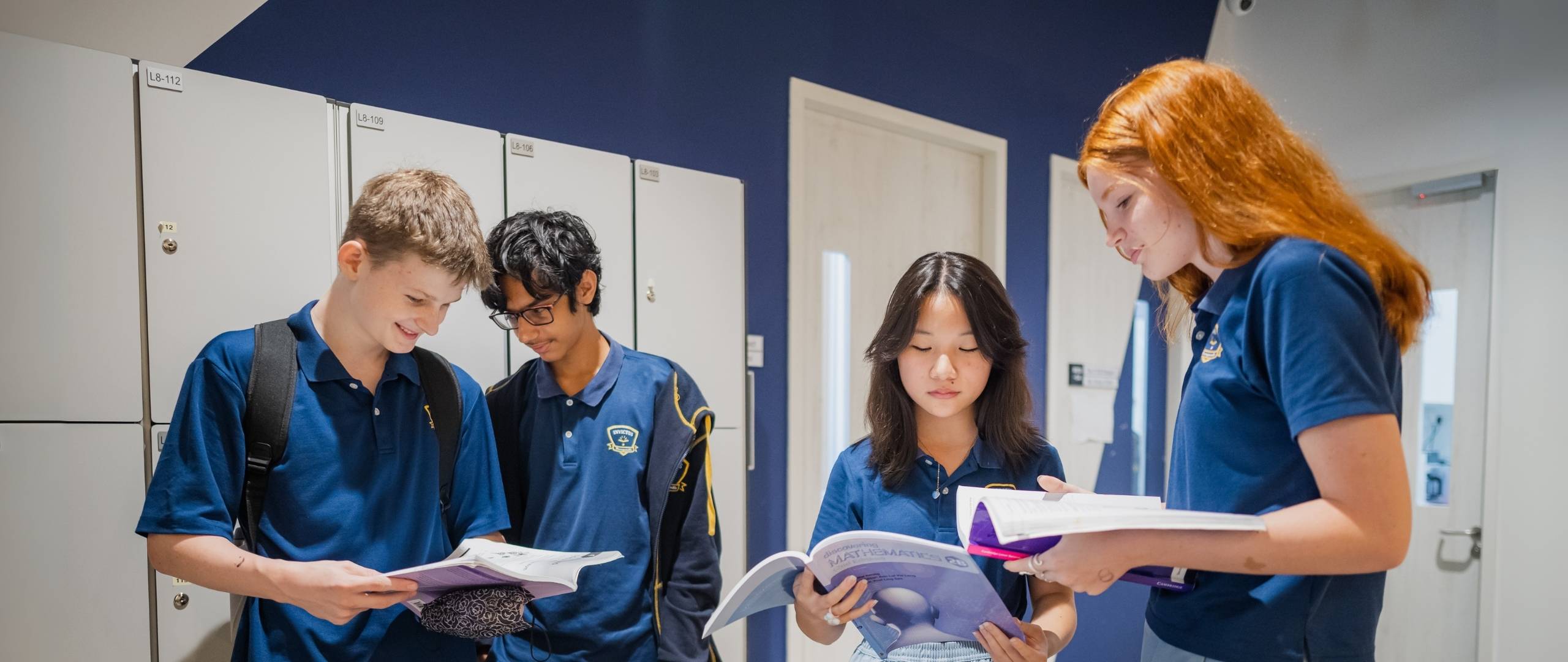 Group of Invictus International School students in Singapore standing by lockers, engaged in reading and discussion, showcasing a collaborative and diverse learning environment.