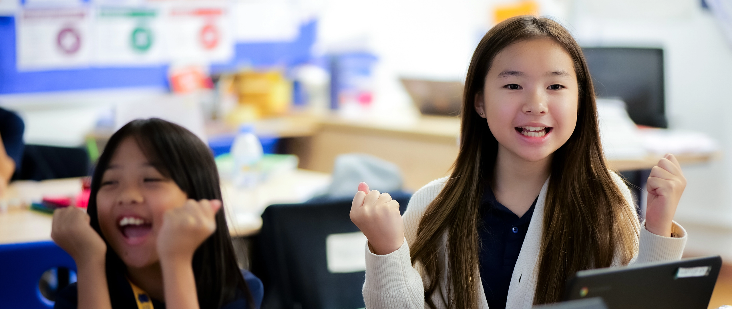 Invictus students cheer joyfully during a classroom activity using laptops, reflecting enthusiasm, engagement, and digital learning success.