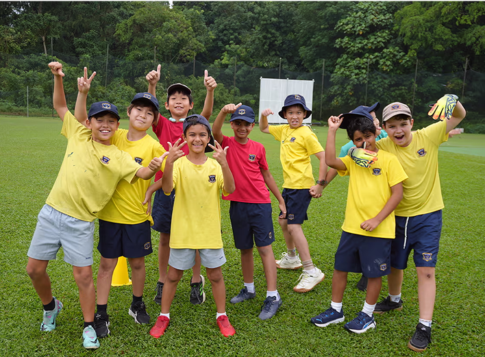 A group of students in bright house-coloured shirts celebrate on a field after participating in an energetic Inter-House sports competition.