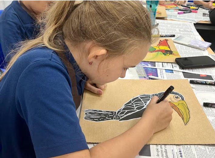A primary student concentrates while outlining a colourful bird design on brown paper during art class at Invictus International School Bukit Timah.