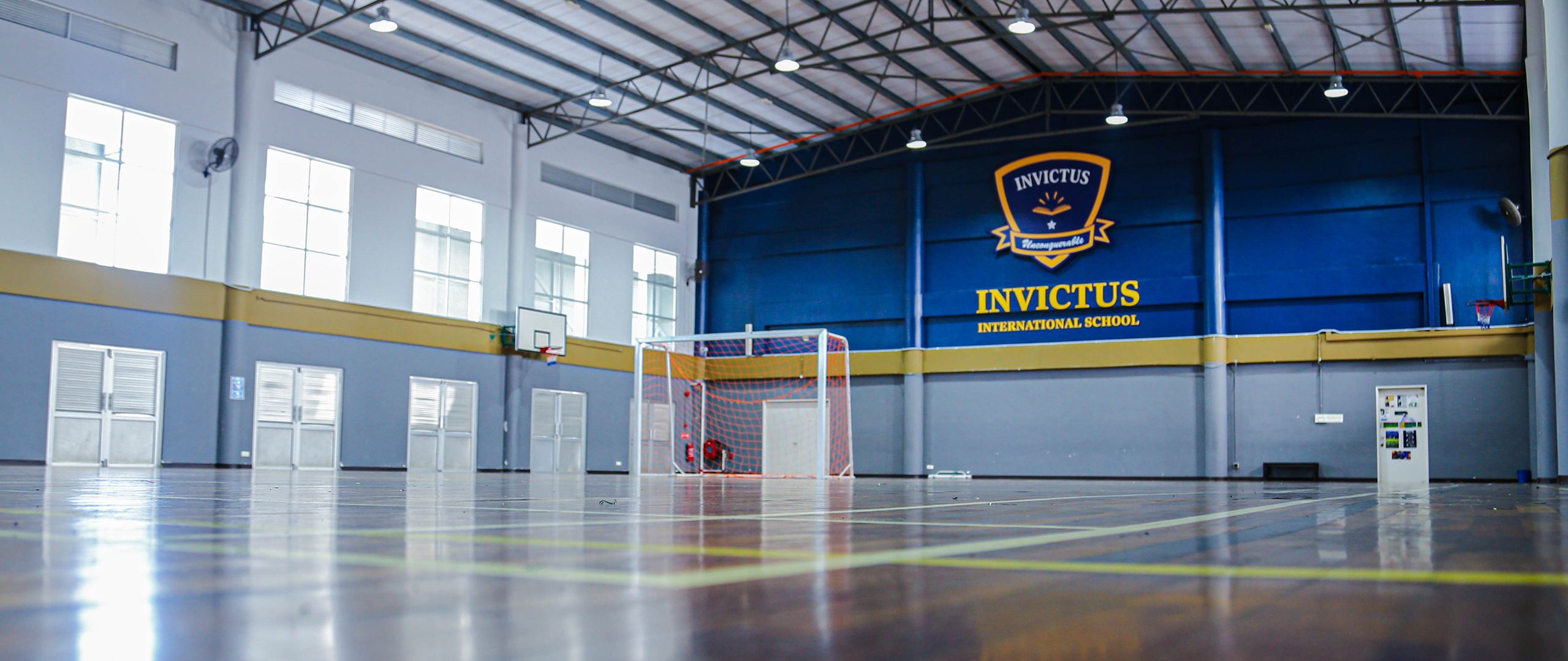 Invictus International School Malaysia Spring Hills Campus indoor sports hall with Invictus logo, futsal goal, and polished wooden floor