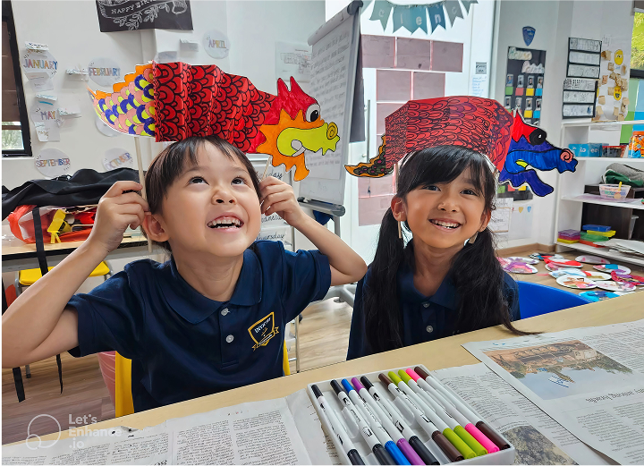 Two cheerful students wearing handmade dragon hats in a cultural arts ECA session at Invictus International School.