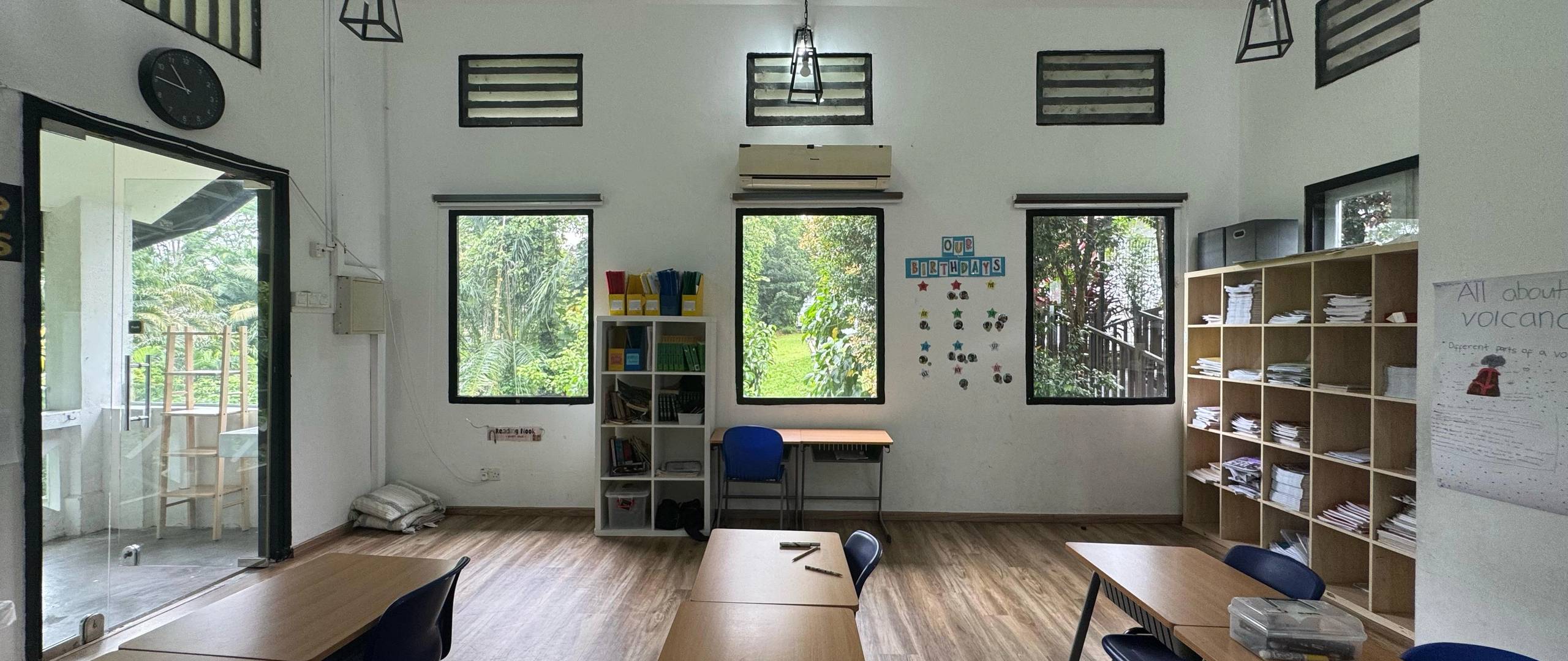 Bright classroom with desks, open shelving, and natural forest views.