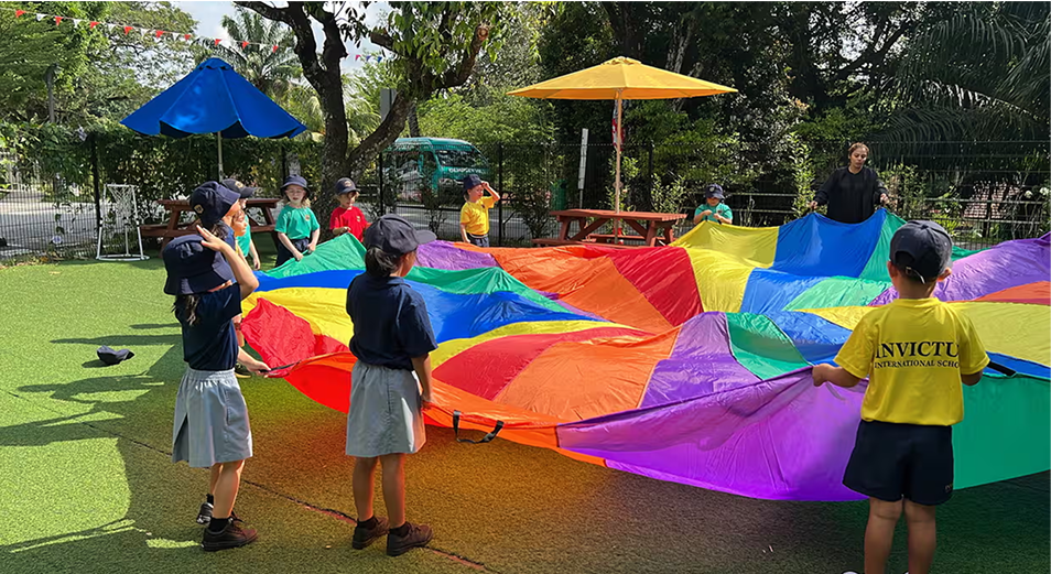 Students engaging in a vibrant outdoor parachute activity at Invictus International School Bukit Timah, fostering teamwork and physical development.