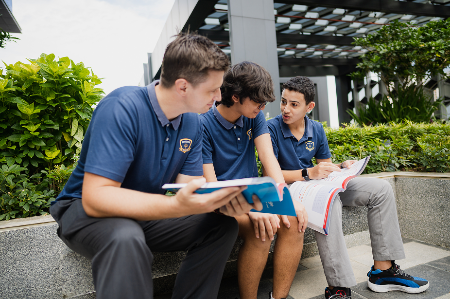 Secondary students discussing books outside with greenery.