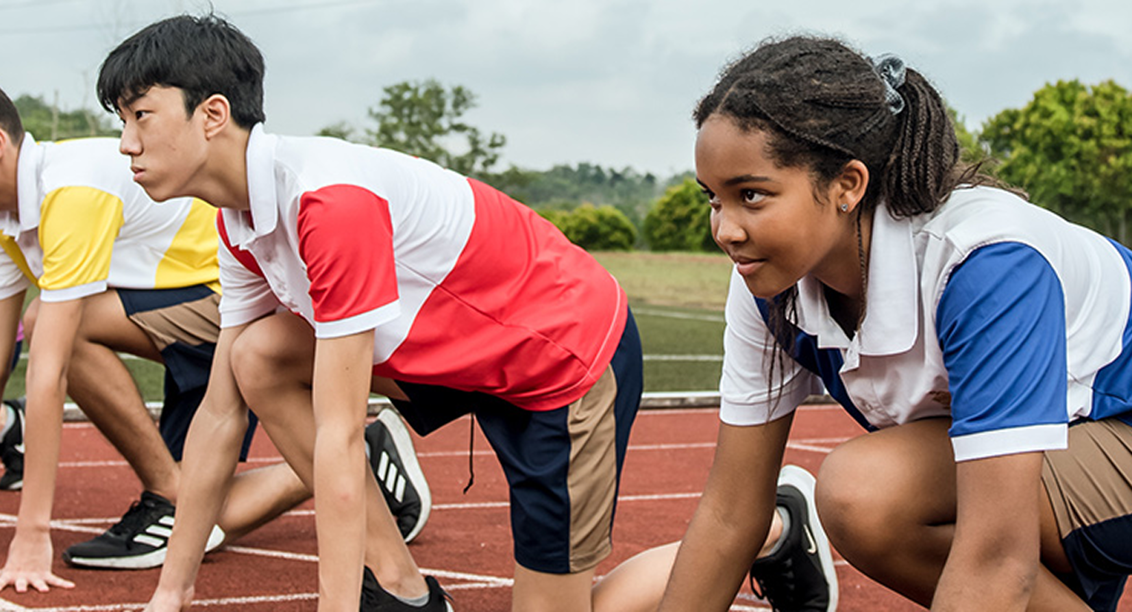 Three students crouched at the starting line, poised to sprint in a House athletics competition.