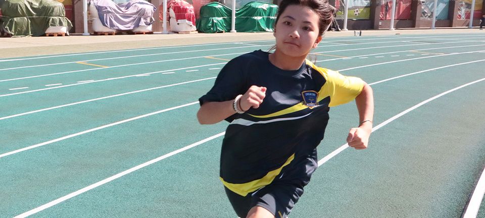 Two Invictus students in navy uniforms seated at a desk, one writing with a pen while the other follows along on a worksheet in a bright classroom.
