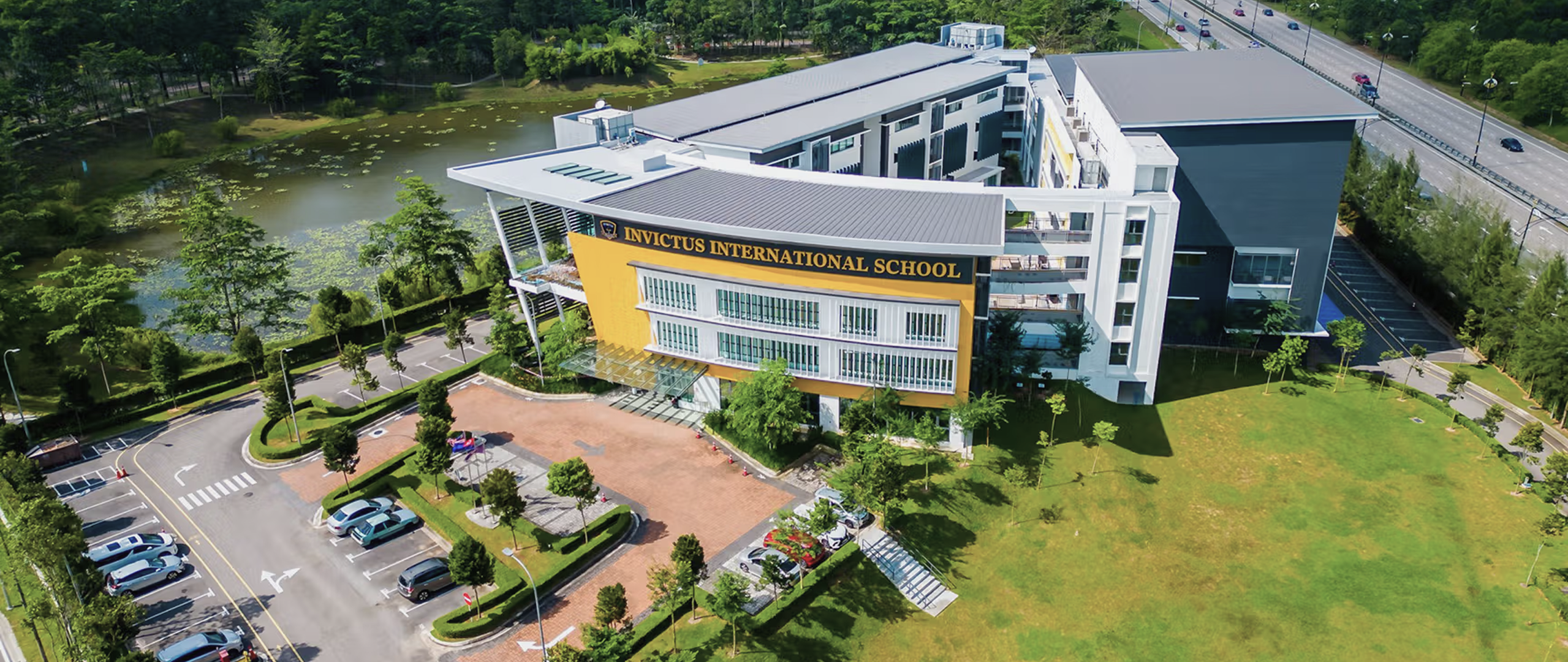 Aerial drone view of Invictus International School Malaysia Spring Hill Campus with vast greenery, parking lot and lake.