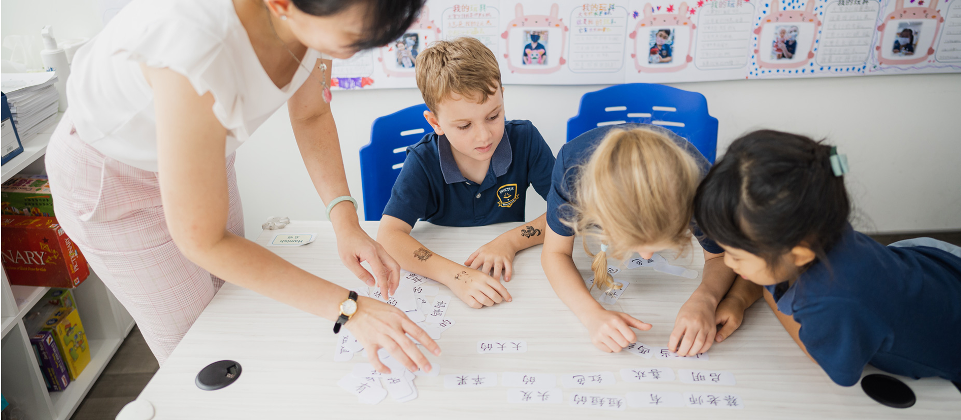 A small group of Year 1–6 students gathered around a table sorting and matching Chinese character cards under the guidance of their Mandarin teacher.