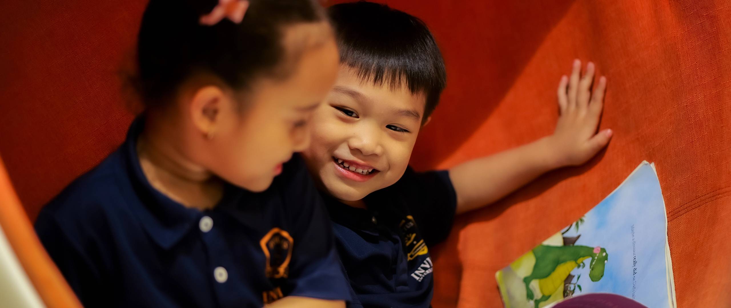 Early years students at Invictus International School explore picture books together at a colourful classroom table, nurturing literacy and friendship