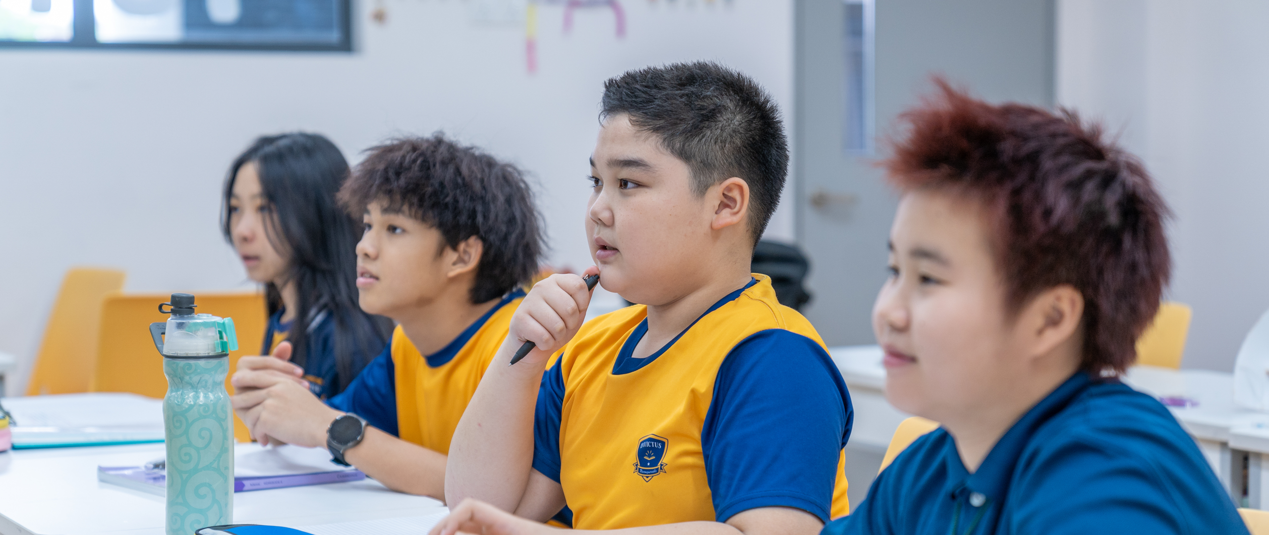 Group of young students in school uniforms holding hands and joyfully jumping together on a grassy field in front of a school building.