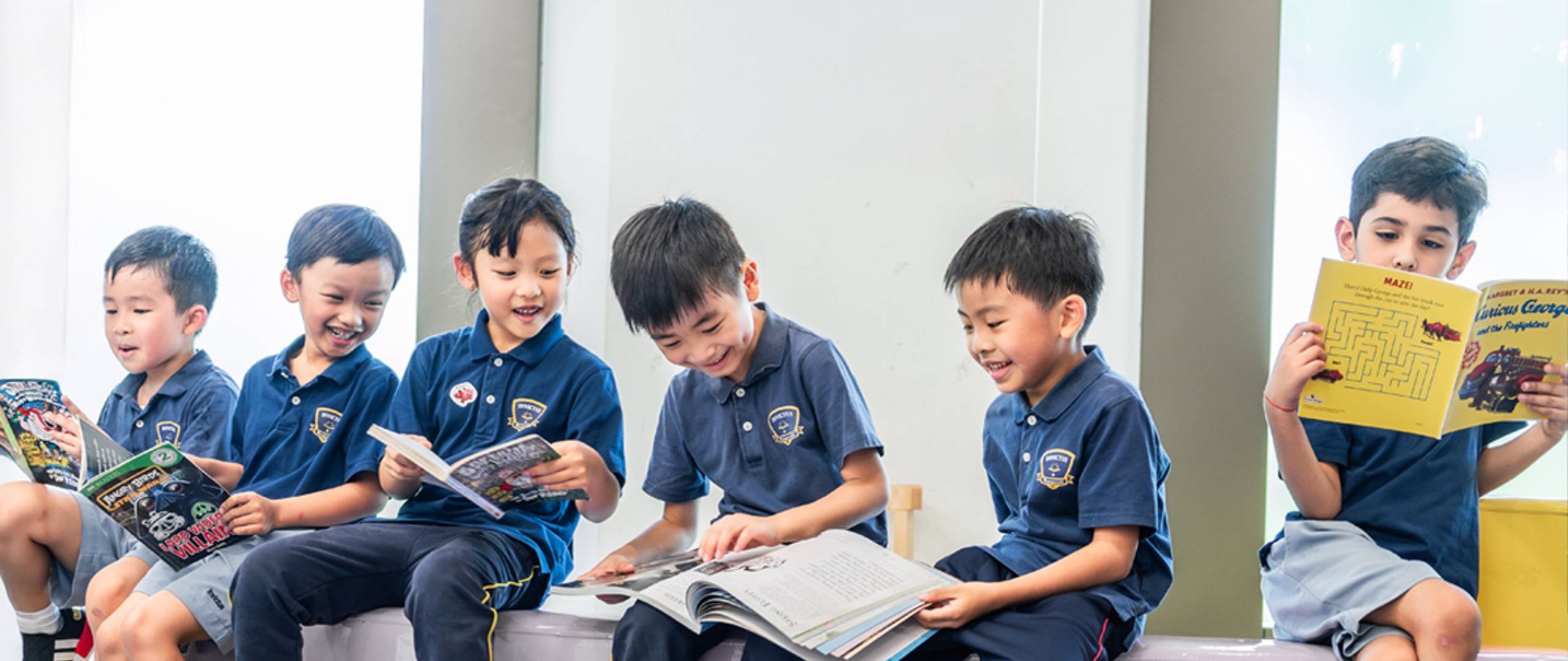 Group of young students in school uniforms holding hands and joyfully jumping together on a grassy field in front of a school building.