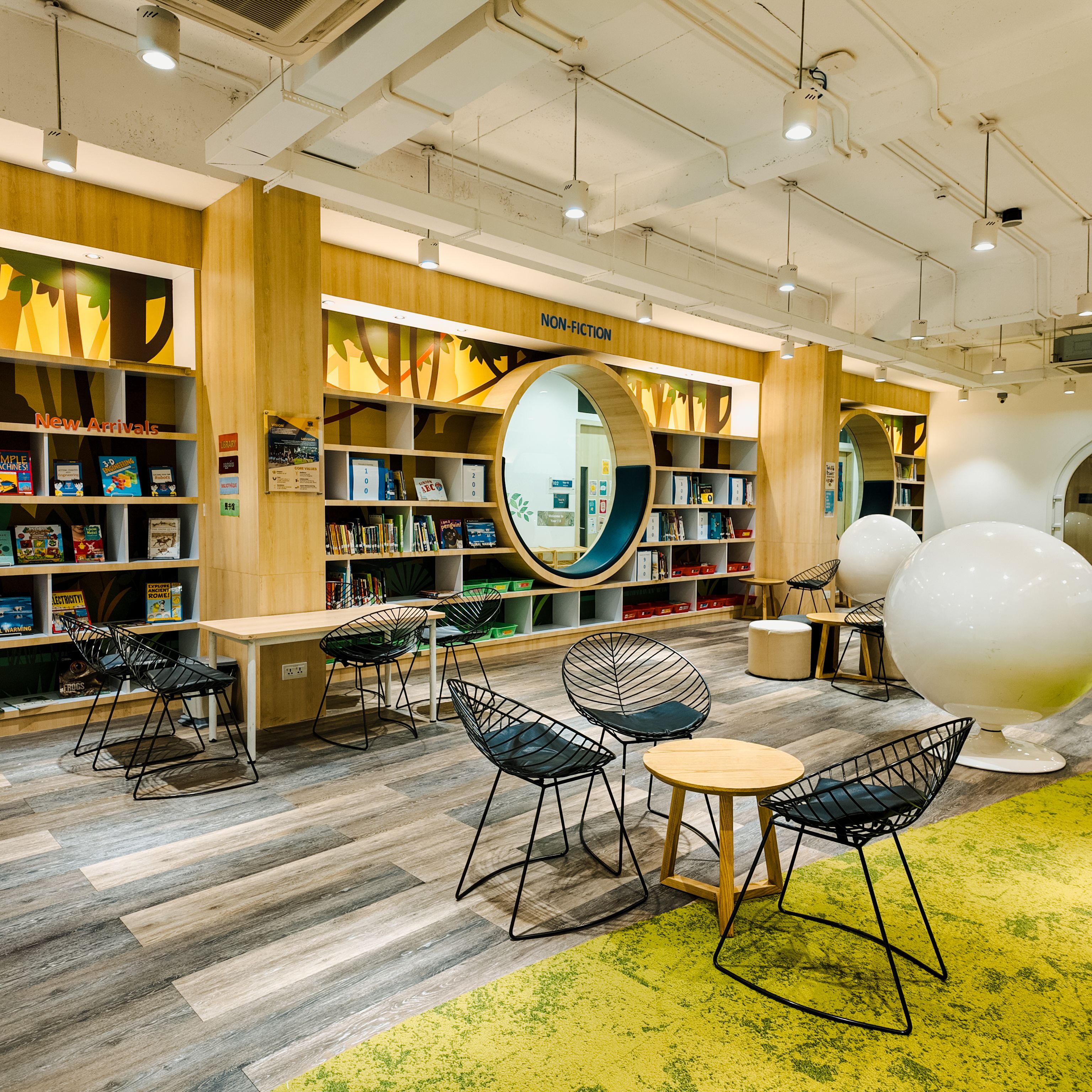 Spacious school library at Invictus Phnom Penh featuring circular reading pods built into the bookshelves, with cosy seating and contemporary furniture creating an inviting learning environment.