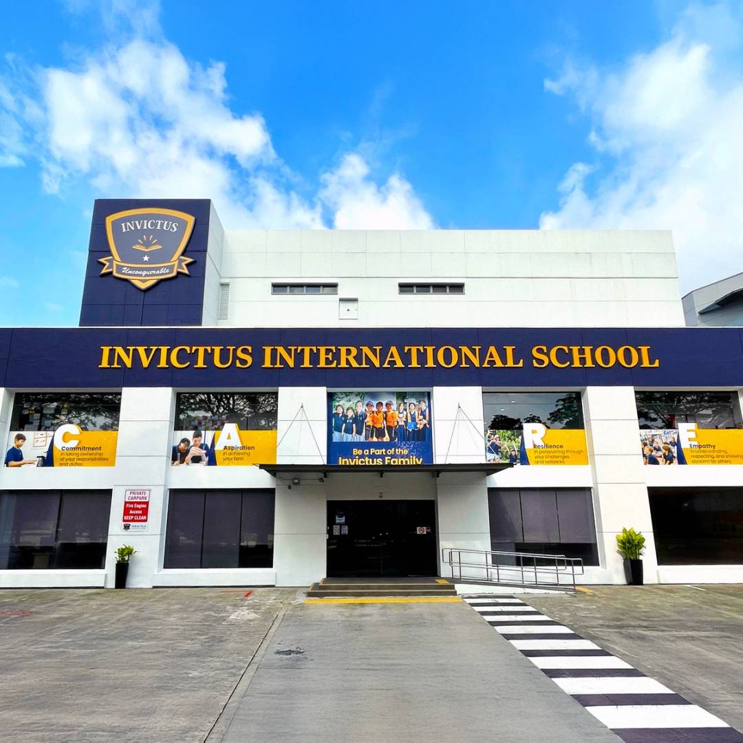 Exterior view of Invictus International School's Bukit Timah Campus in Singapore, showcasing a modern grey and navy-blue building with bold yellow signage under a bright sky.