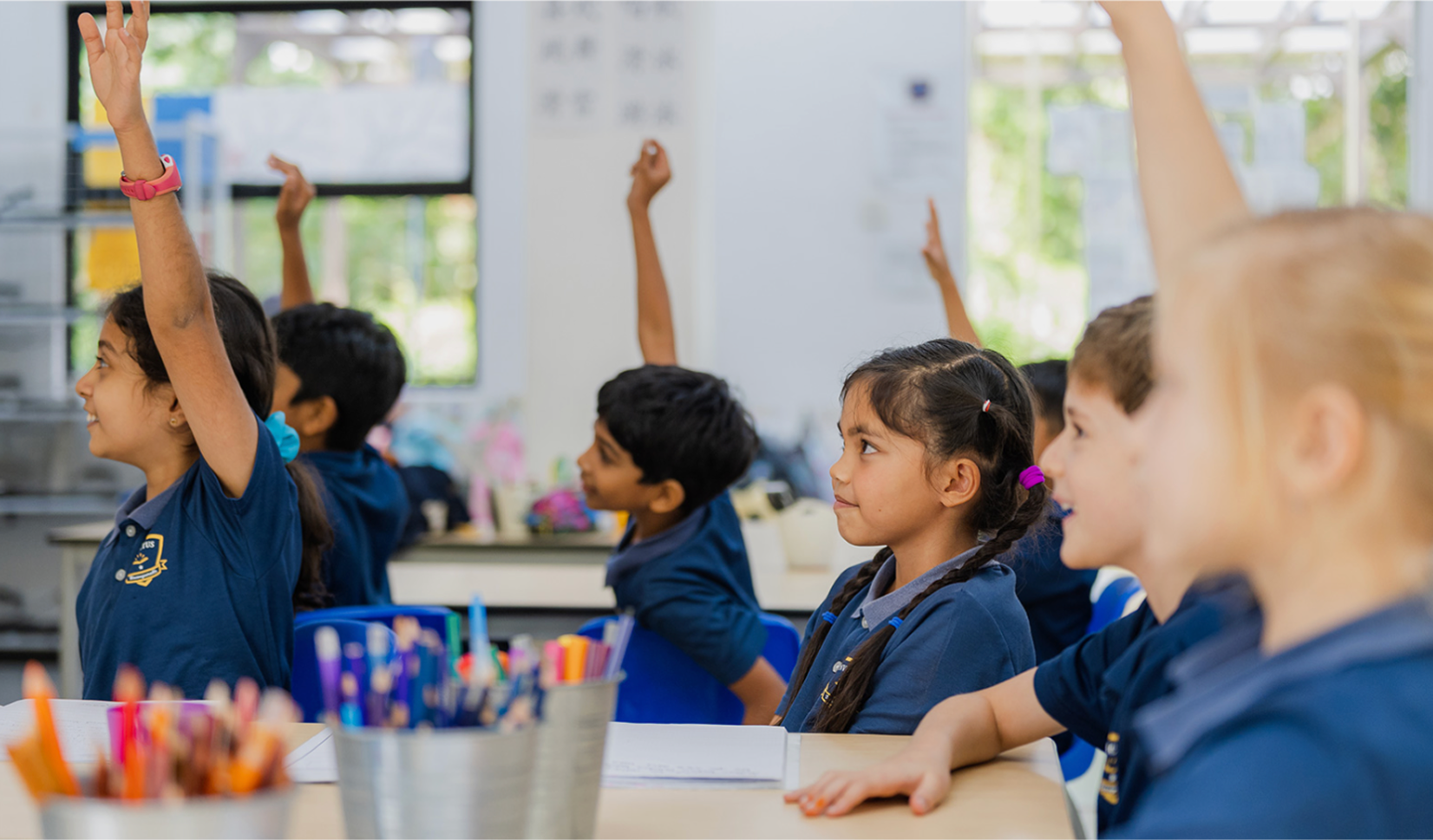 Primary students at Invictus International School Bukit Timah raising their hands in an engaging classroom, showing confidence and active participation in learning.