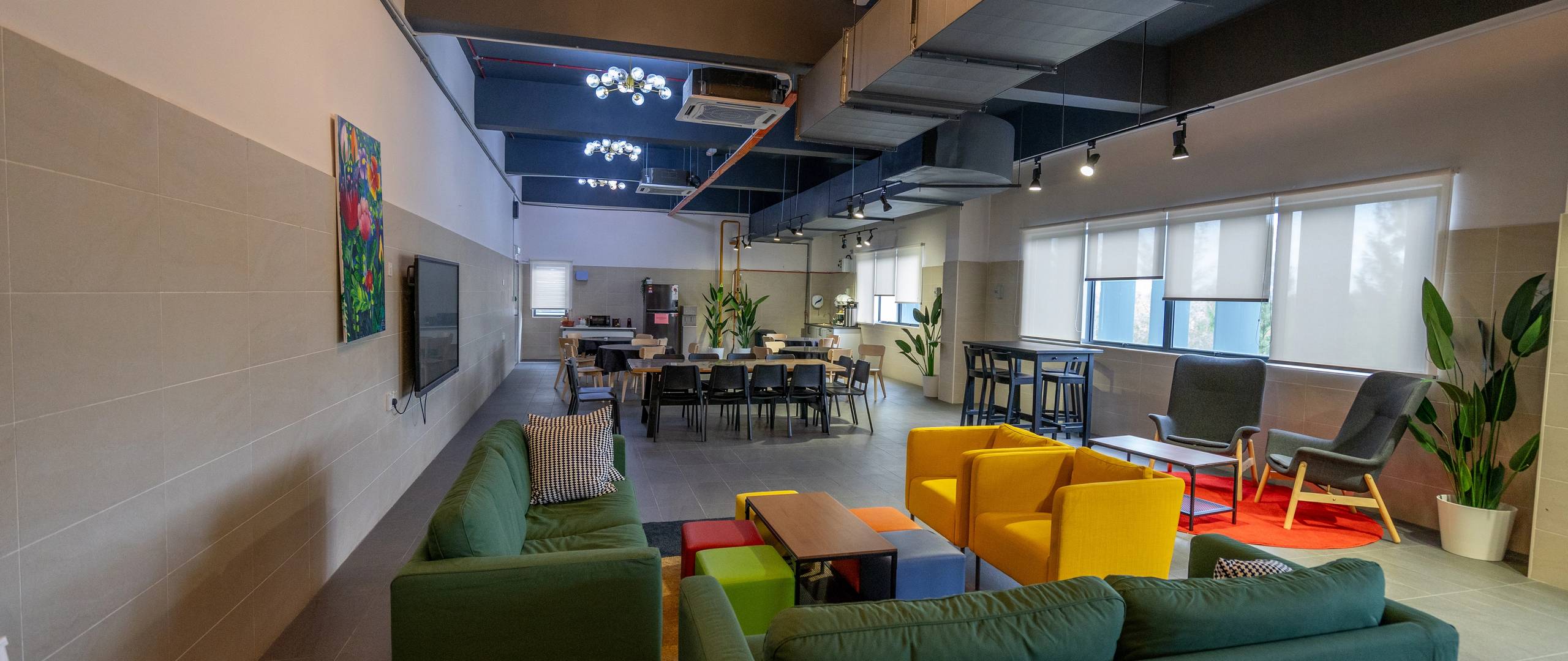 Student lounge with comfy sofas, dining tables, and greenery.