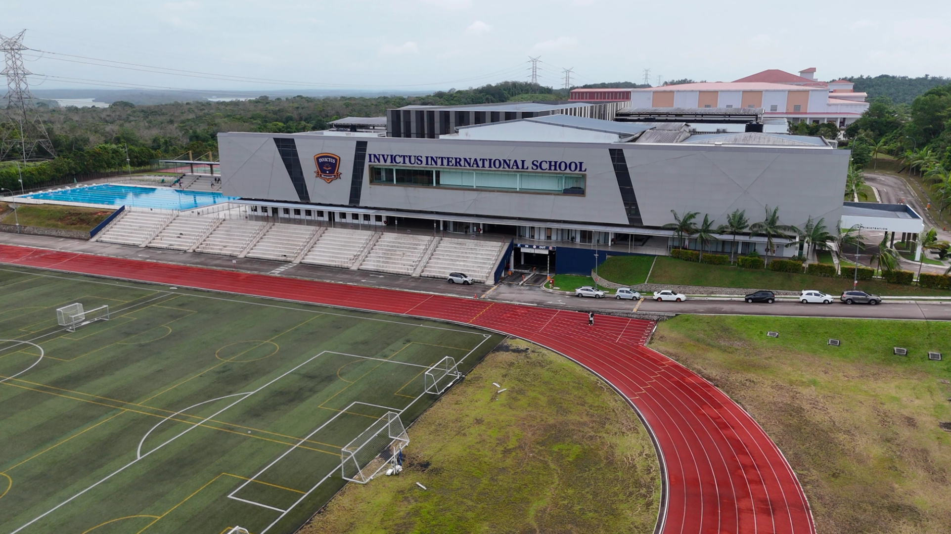 Aerial view of Invictus International School’s Spring Hills Campus in Malaysia, featuring a large swimming pool, running track, tennis courts, and multiple modern academic buildings surrounded by greenery.