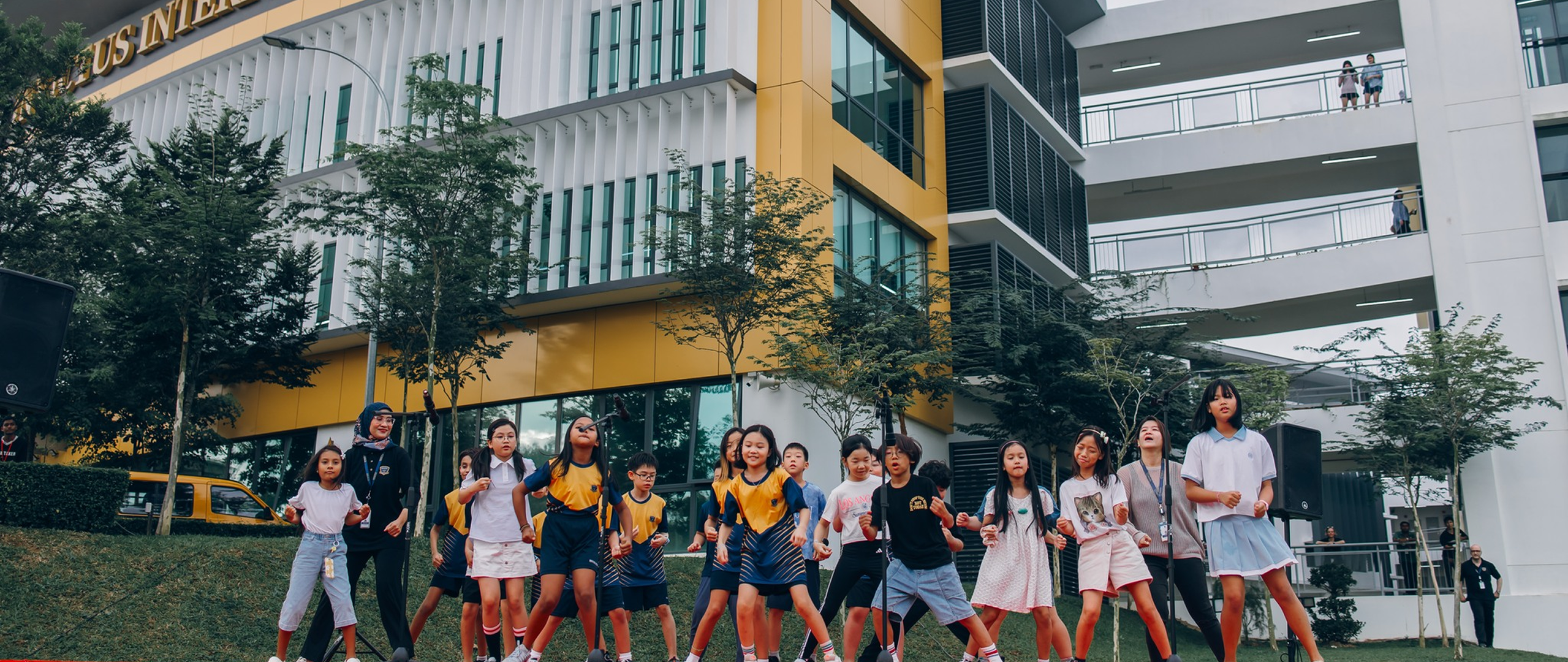 Students and staff participating in outdoor activities in front of the Invictus International School campus building, with the school's yellow and white facade visible in the background.
