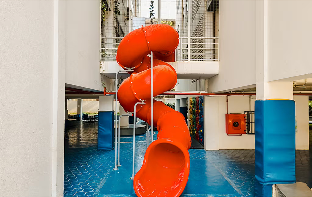 Striking red spiral playground slide set between school buildings at Invictus Phnom Penh, offering a fun and active break-time option for students.