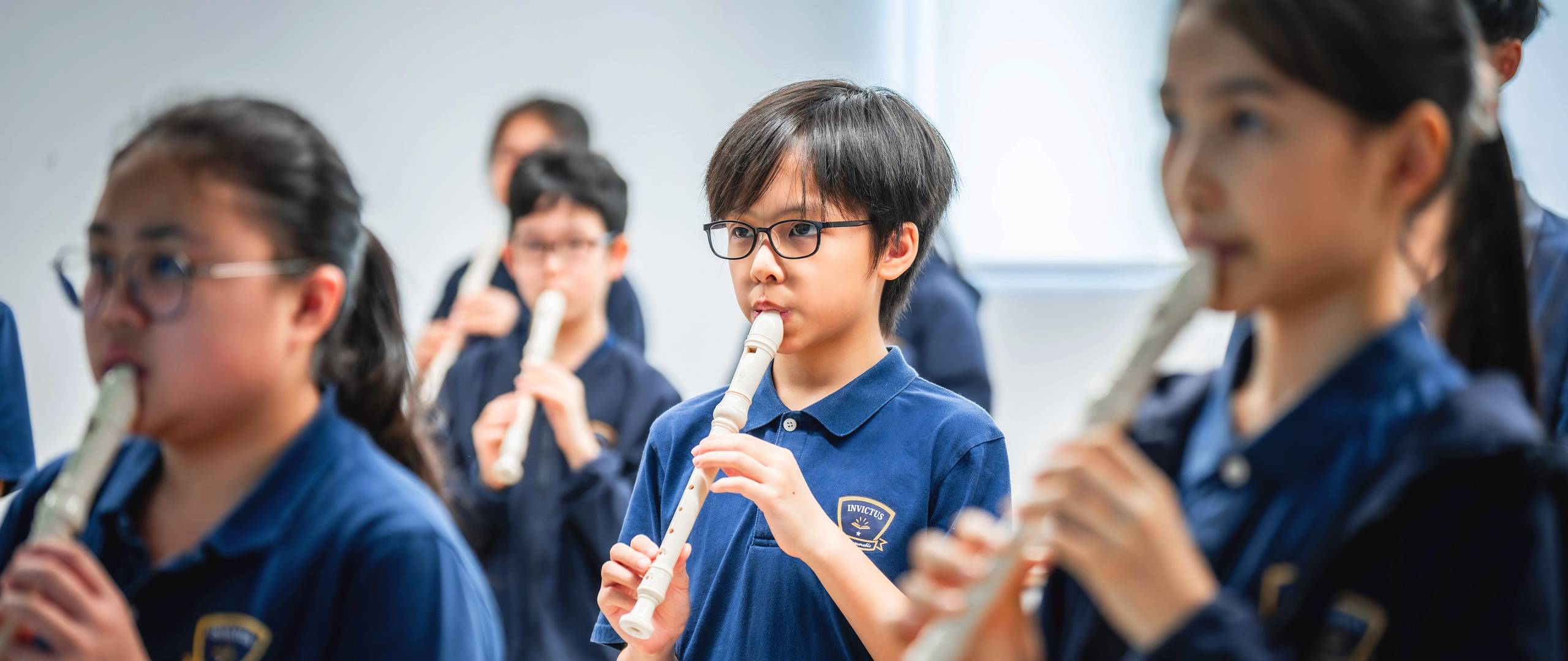 Group of young students in school uniforms holding hands and joyfully jumping together on a grassy field in front of a school building.