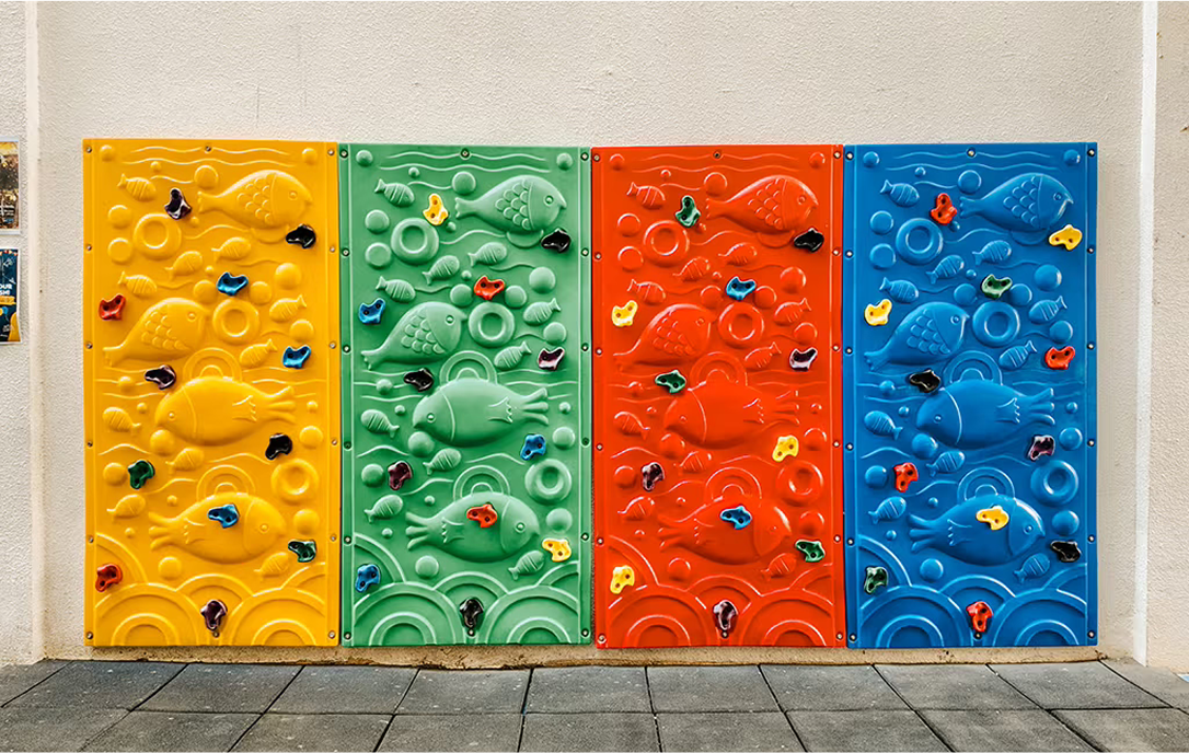 Four vibrant climbing wall panels in yellow, green, red, and blue, each embossed with underwater sea creatures, designed for outdoor student play at Invictus Phnom Penh.