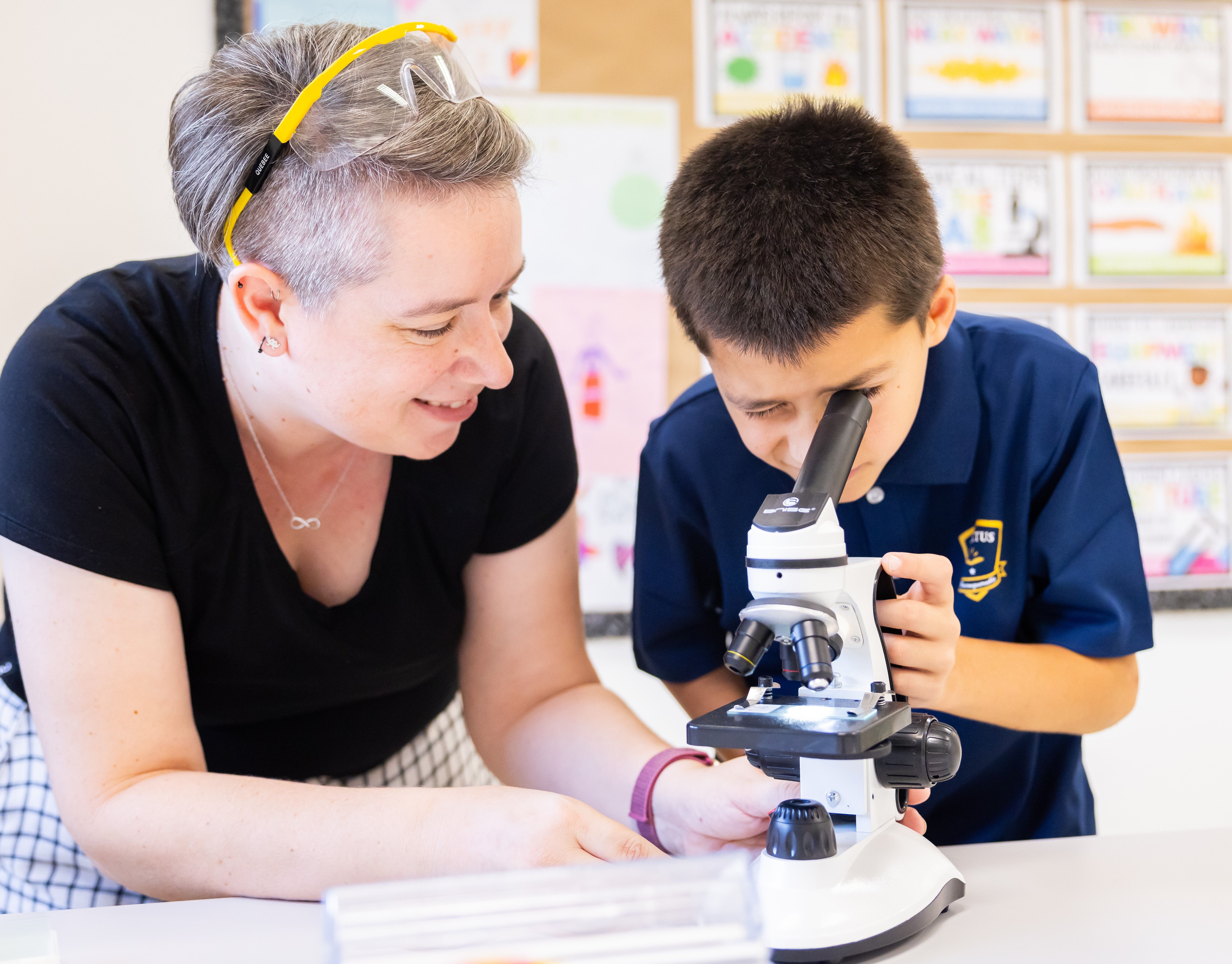 Invictus Bukit Timah student using a microscope with teacher guidance during a science lab activity.