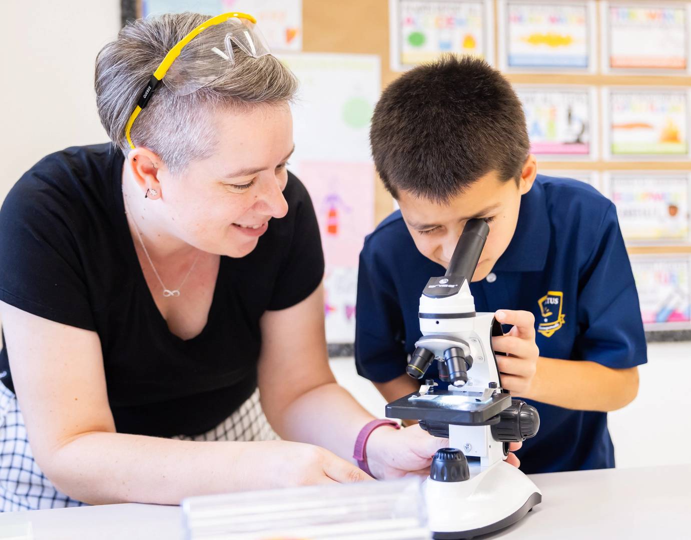 Invictus Bukit Timah student using a microscope with teacher guidance during a science lab activity.