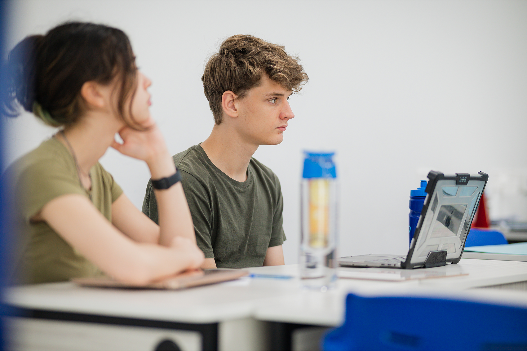 Sixth form students at Invictus Singapore attentively engaged in a Cambridge A-Level class using digital devices and notebooks, reflecting academic focus and university preparation.
