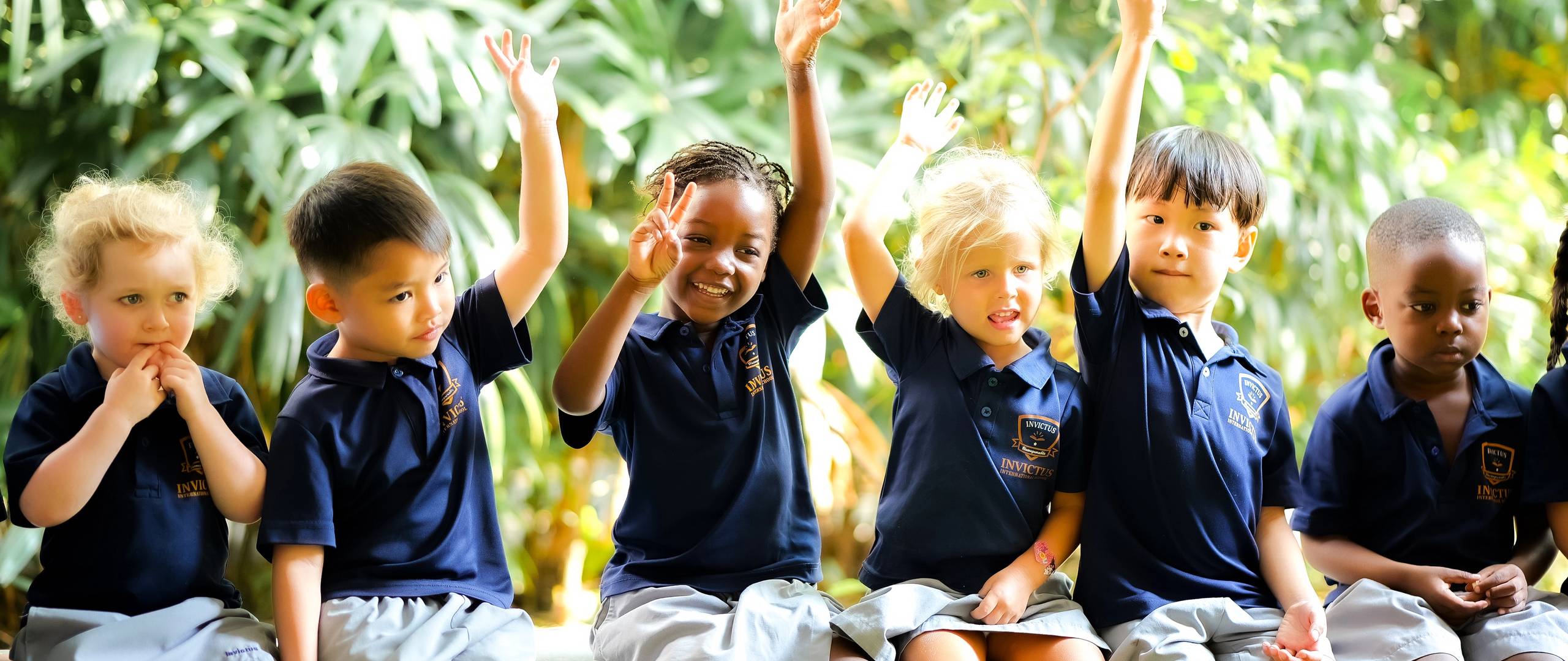 Invictus students from diverse backgrounds raise their hands enthusiastically during an outdoor learning session, showing engagement and confidence.