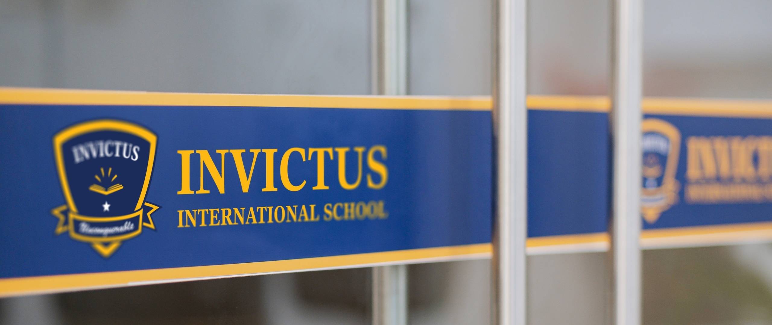 Close-up of the Invictus International School logo and branding on a glass door, featuring the blue and gold school crest and bold yellow text.