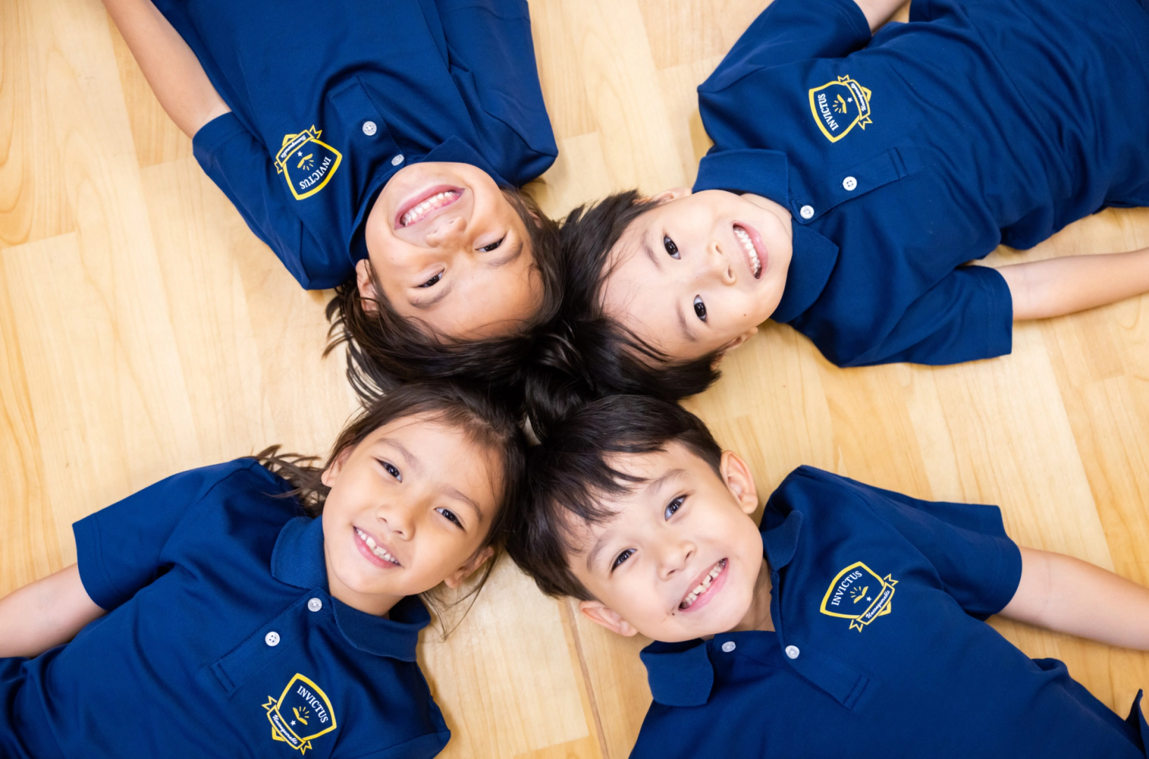Four students lying down on the wooden floor smiling at the ceiling