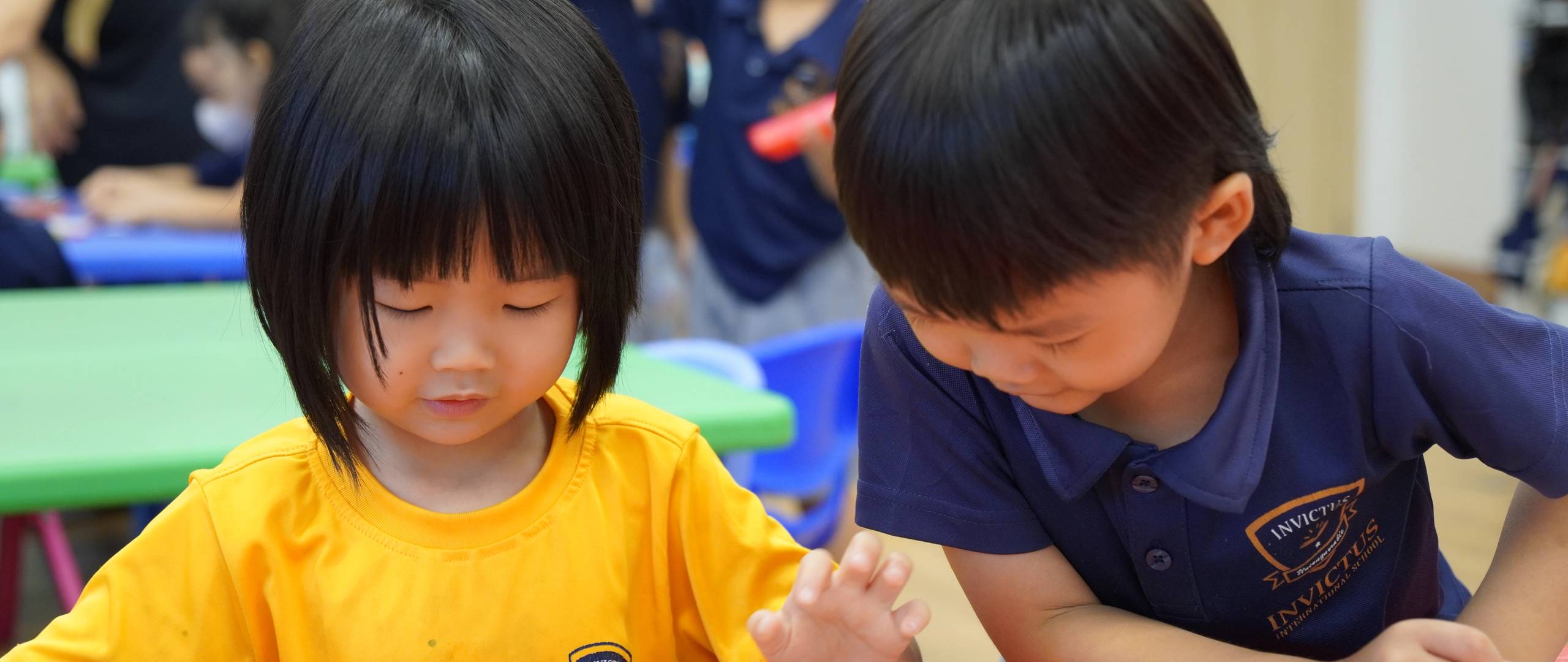 Early years students at Invictus International School explore picture books together at a colourful classroom table, nurturing literacy and friendship.