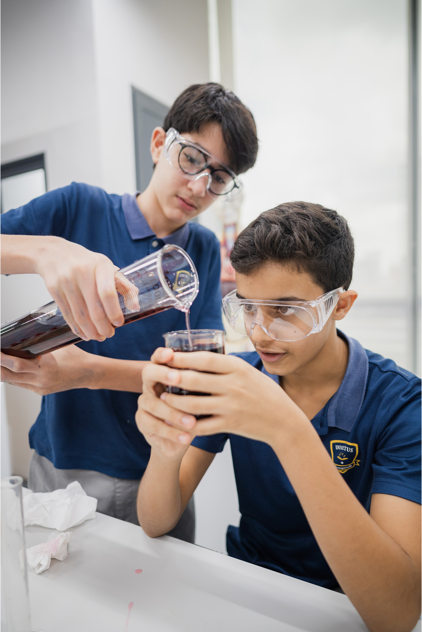 Cambridge A-Level students at Invictus International School Singapore conducting a hands-on science experiment with measuring cylinders and safety goggles in a modern laboratory.