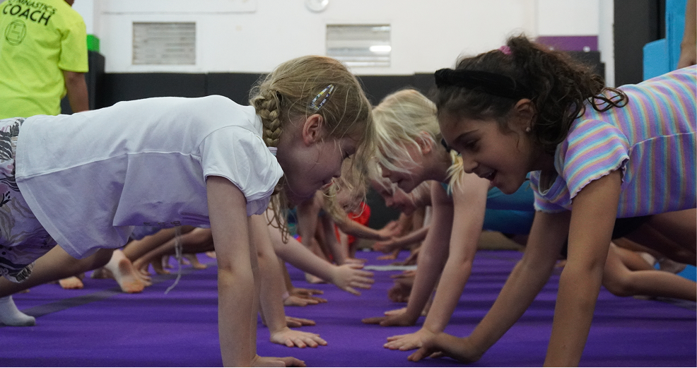 Students face each other in a push-up challenge during a gymnastics ECA session, developing strength and teamwork.