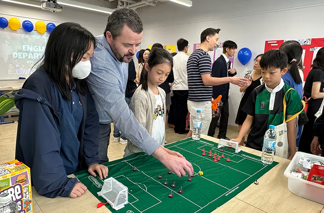 A teacher and students discussing football strategy on a fabric pitch on a table.