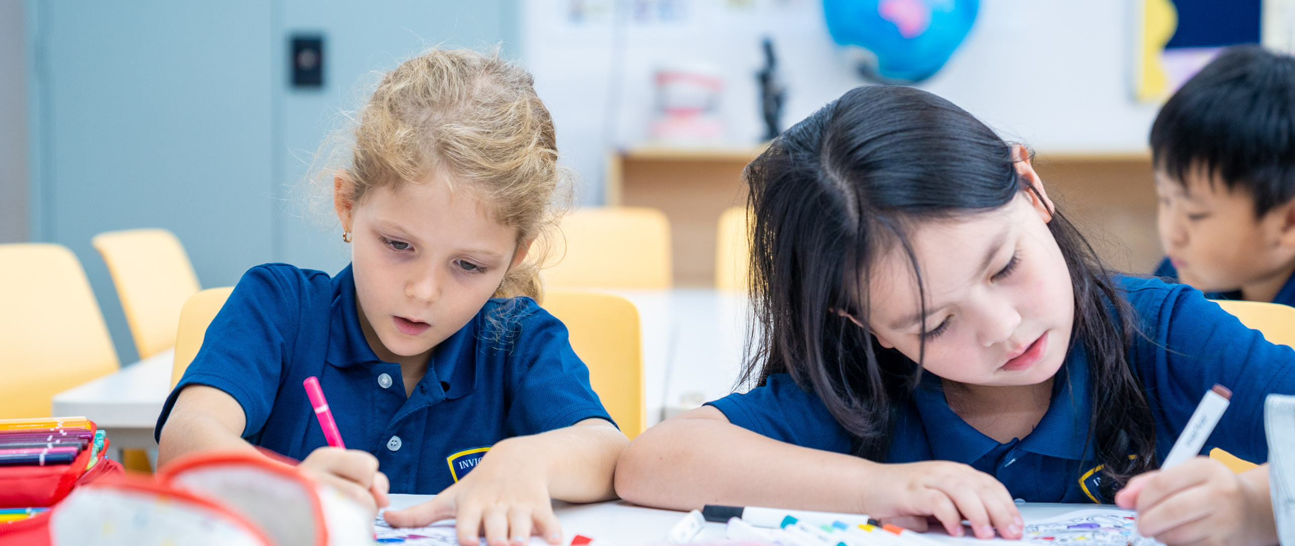 Group of young students in school uniforms holding hands and joyfully jumping together on a grassy field in front of a school building.