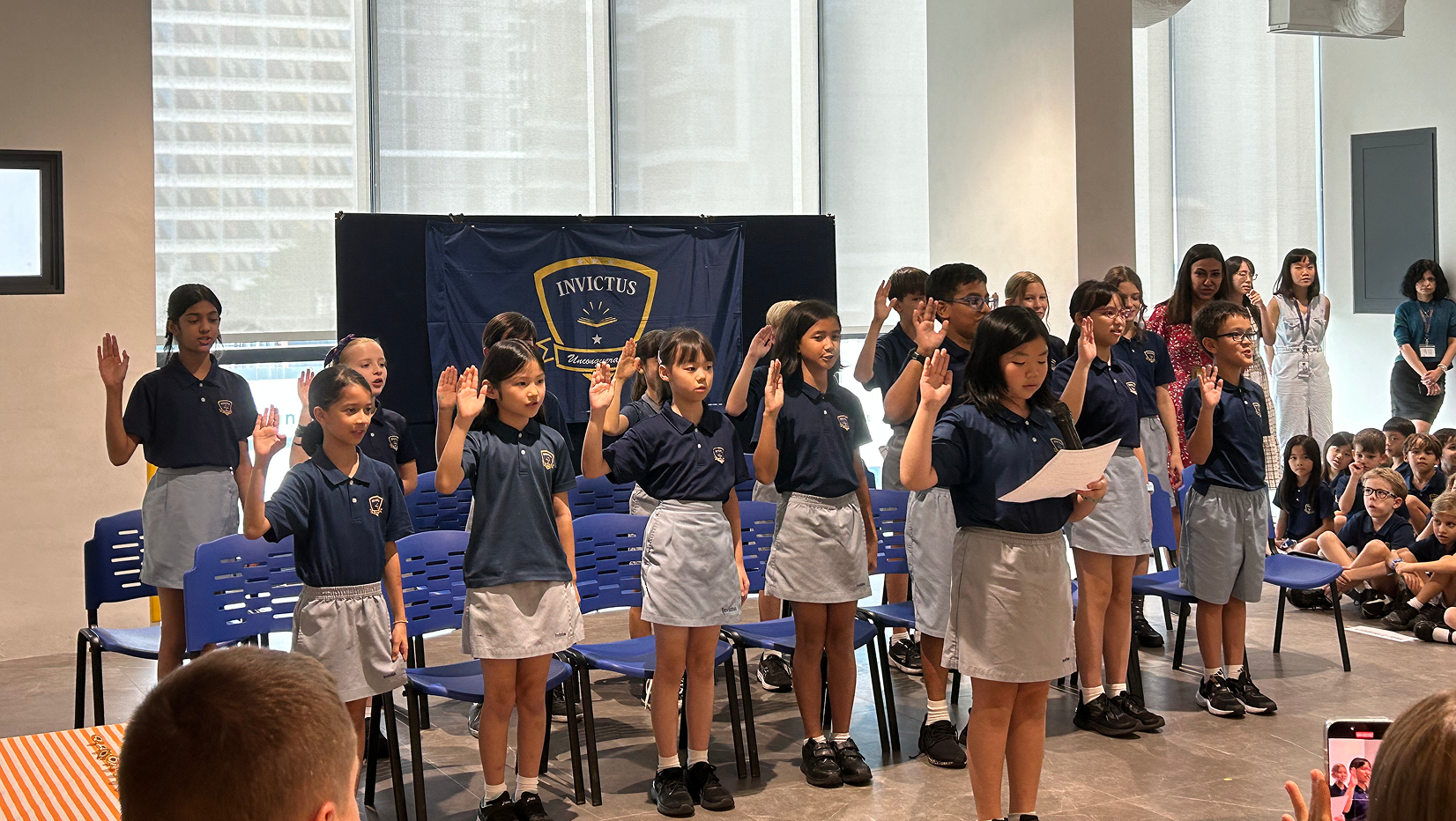 Students from Invictus International School raise their hands to take an oath during the Student Council induction ceremony, with peers and staff watching in support.