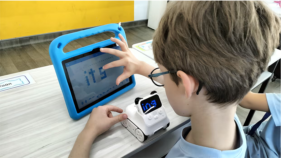 A student uses a tablet to control a small white robot, working on digital literacy and coding skills in a technology-focused ECA session.