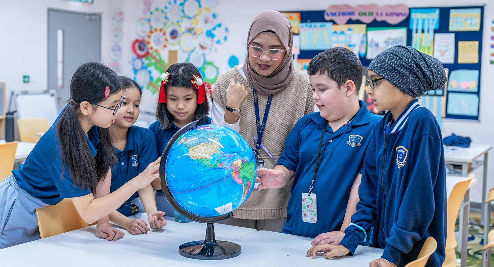Primary students at Horizon Hills Invictus International School Malaysia exploring a globe with their teacher, engaging in interactive learning.