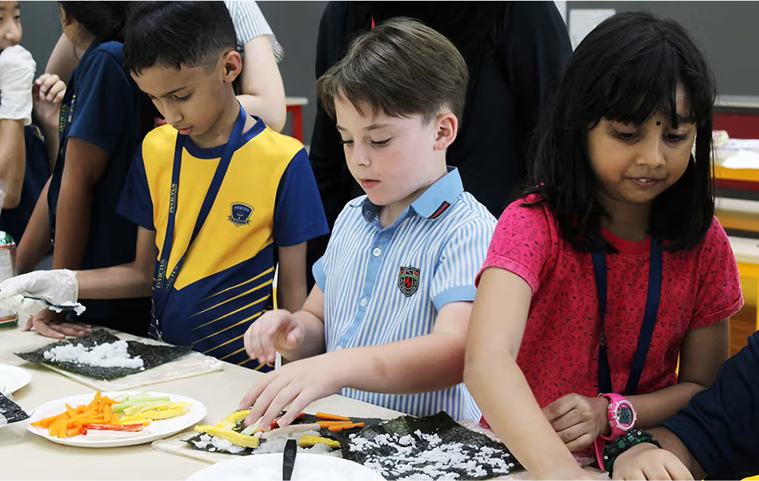 Primary students preparing sushi during a cultural cooking activity, developing culinary skills and cultural awareness through experiential learning.
