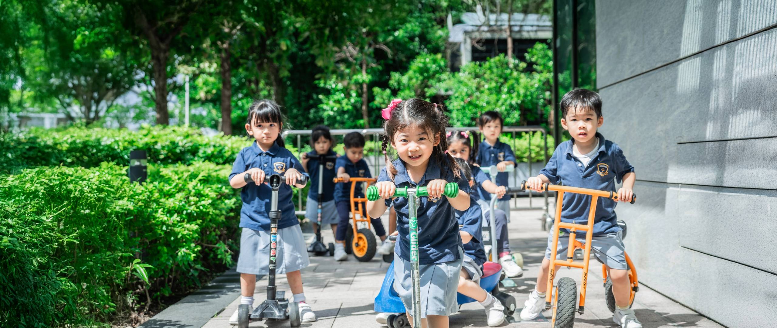 Group of young students in school uniforms holding hands and joyfully jumping together on a grassy field in front of a school building.