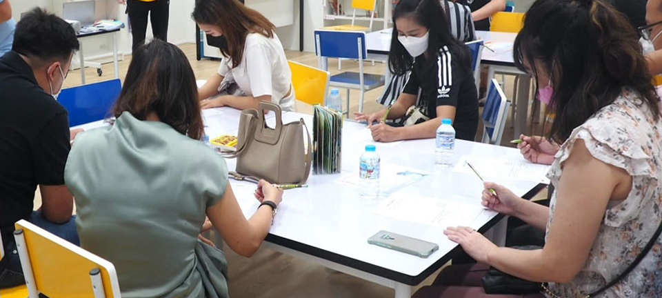 Parents seated at a white classroom table, filling out forms and consulting with Invictus staff during a campus tour session.