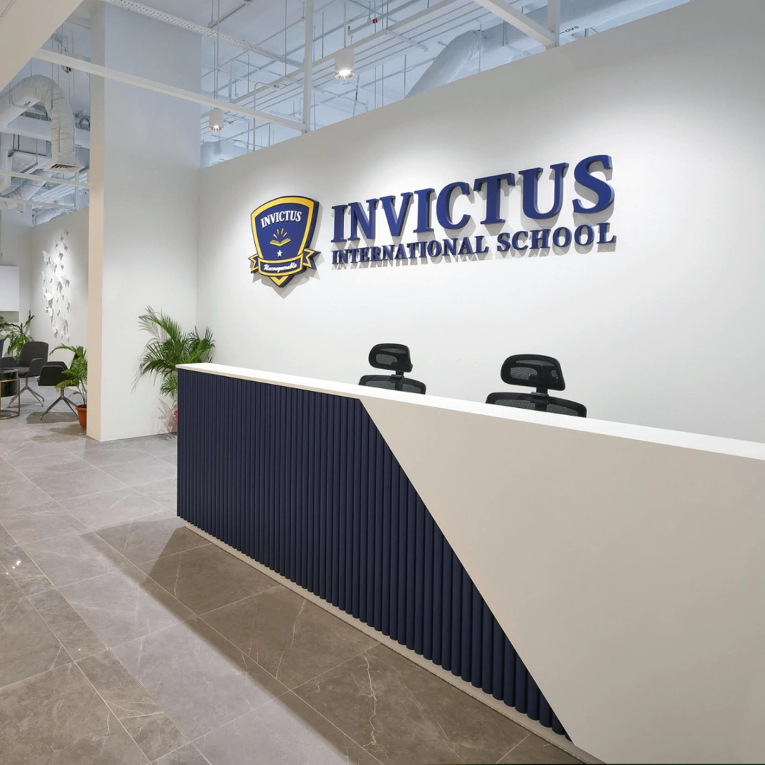 Reception area of Invictus International School's Centrium Square Campus in Singapore, featuring a modern front desk, school logo on the wall, indoor plants, and a contemporary waiting lounge.